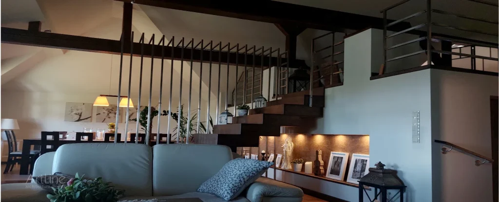 Projekt salonu i jadalni na poddaszu w domu jednorodzinnym powyżej 100m2 w stylu modern rustic – ciemna podłoga i belki konstrukcyjne kontrastują z metalową balustradą